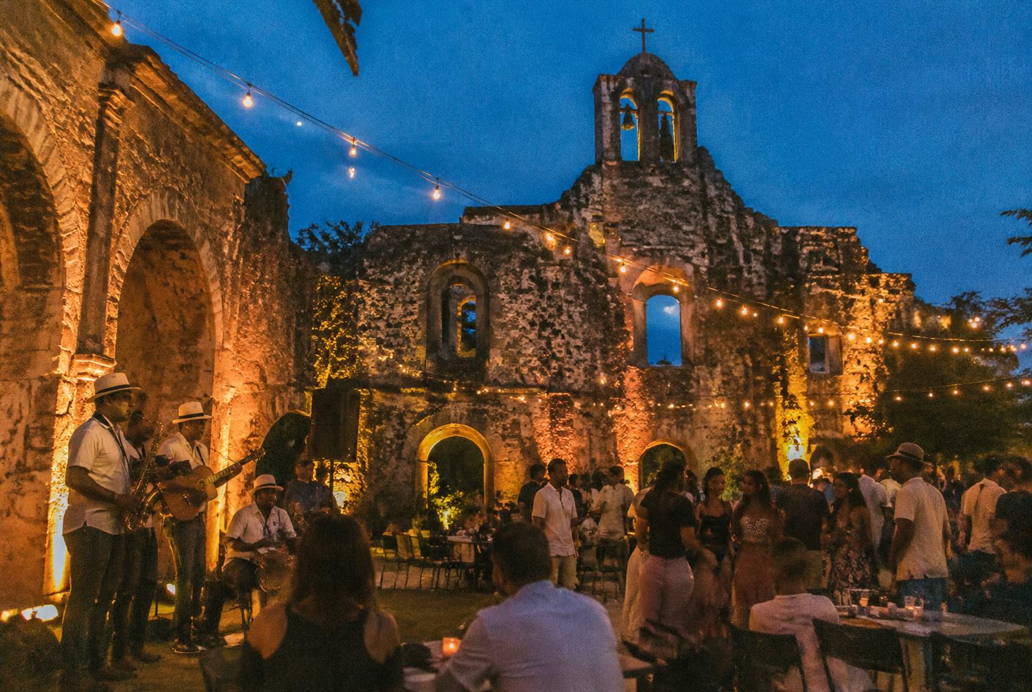 Musicians playing beneath string lights at stone colonial ruins at dusk