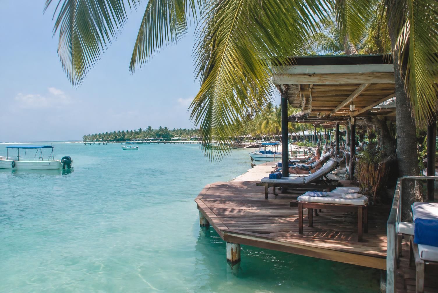 Wooden beach club deck over shallow turquoise water under palms